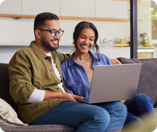 Smiling couple sitting on couch using laptop to review insurance options